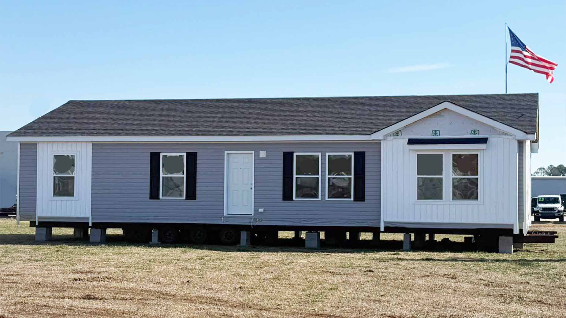 A gray modular home with white trim and an American flag on the roof, sitting on a grassy lot.
